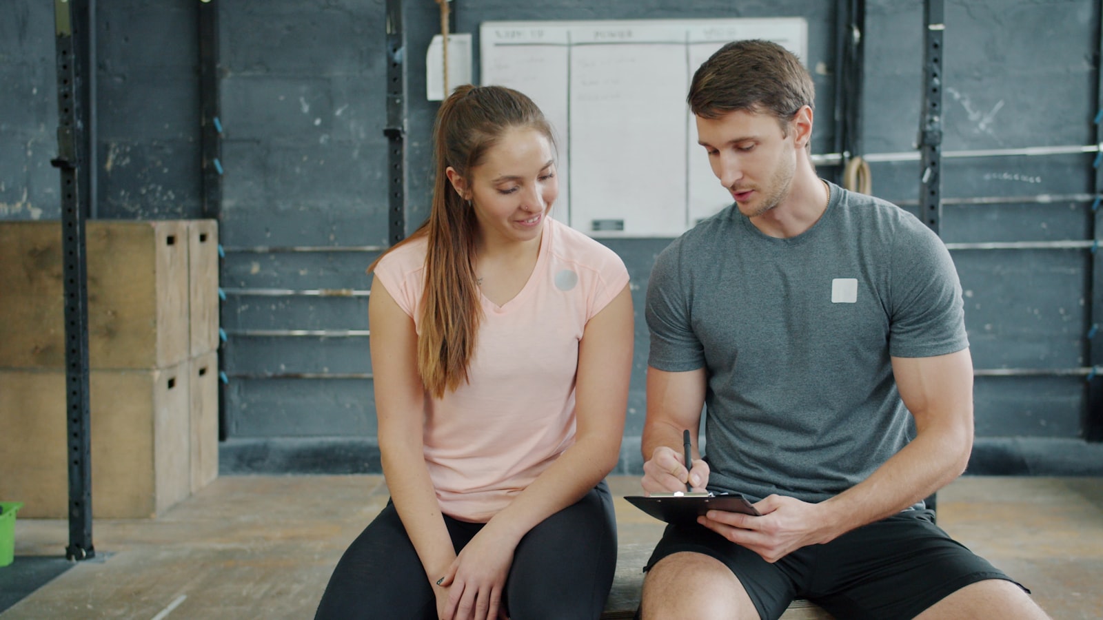 Personal trainer a escrever um plano de treino numa prancheta com uma aluna